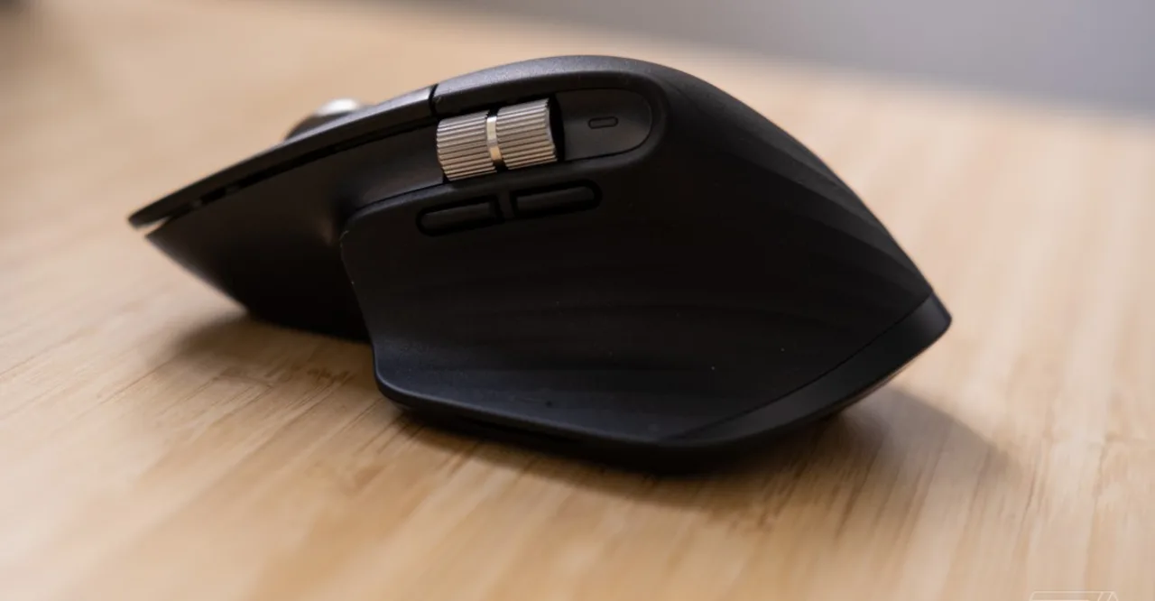 Jovem sentado em cadeira ergonômica, usando mouse Logitech MX Master 3S ao lado de garrafa d'água e halteres