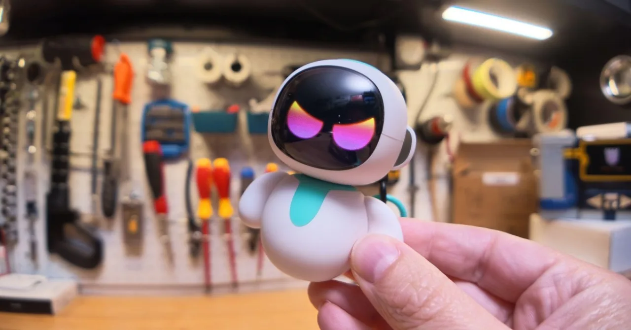 Robô de bolso Eiliko ao lado de um escudo de segurança digital, com códigos binários ao fundo