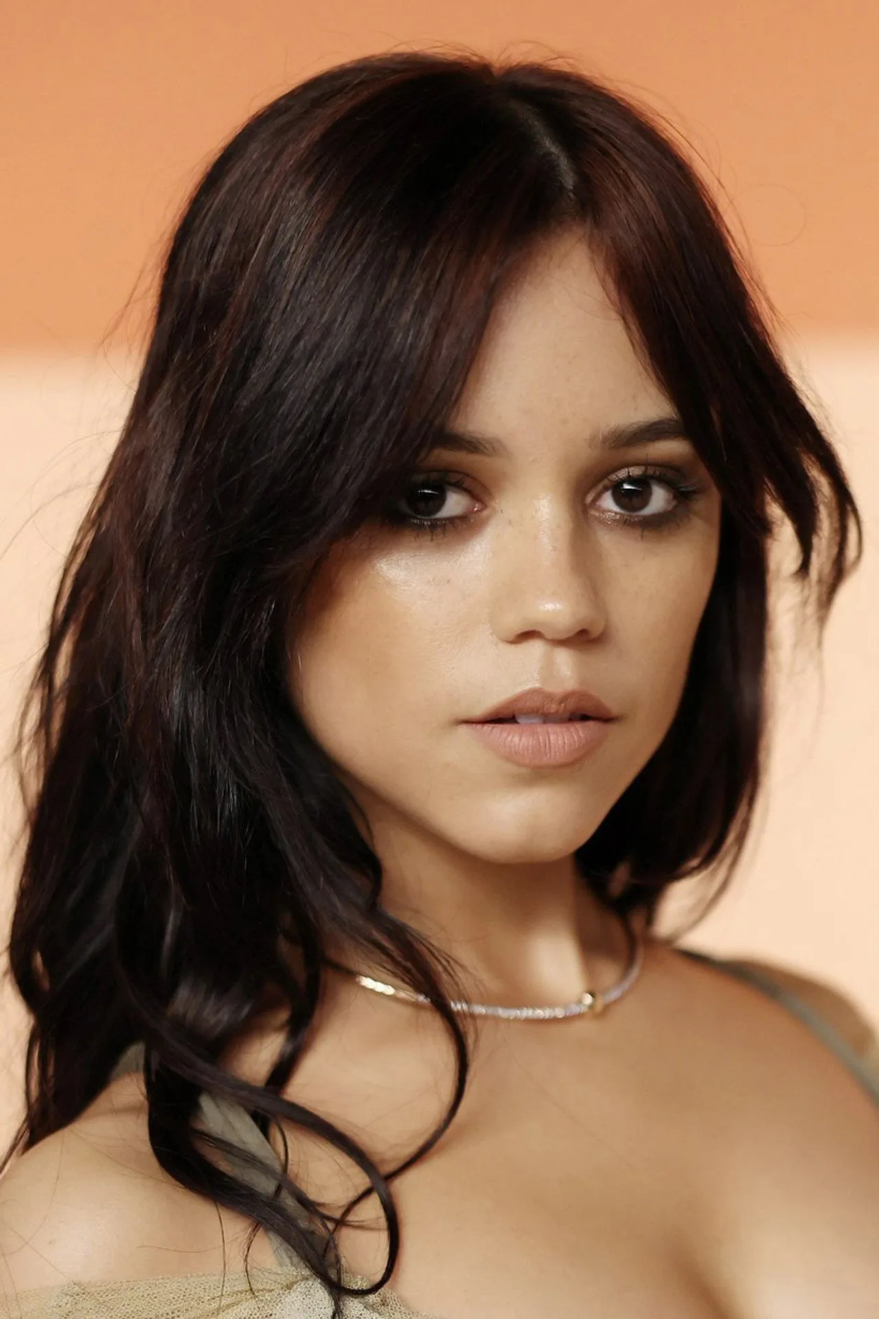 Jenna Ortega vestindo roupa de treino, segurando um copo de água ao lado de um tapete de yoga e halteres