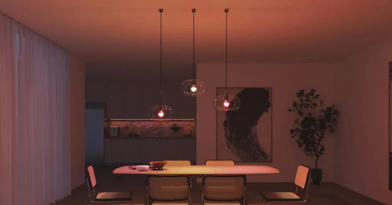 Sala moderna iluminada por lâmpadas Philips Hue coloridas, com sofá, planta e controle inteligente ao lado
