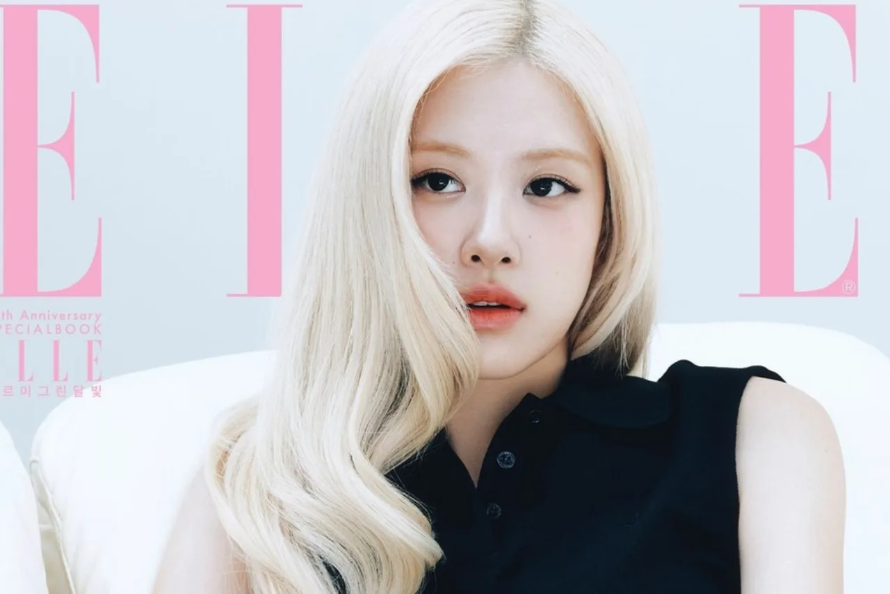 Rosé vestindo roupa esportiva rosa, fazendo alongamento ao ar livre, com garrafa d’água e toalha ao fundo