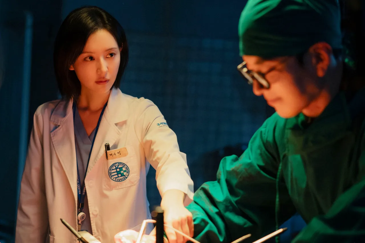 Cena de Doctor X com o médico em jaleco, fundo de hospital e o logotipo da série ao lado