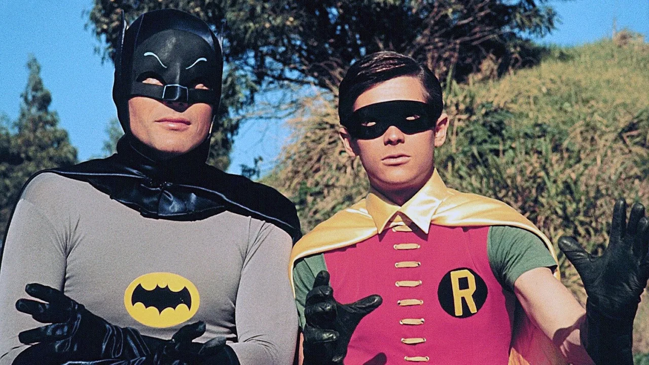 Atleta segurando halteres ao lado de gibis do Batman, Demolidor e Ben 10, uma garrafa de água e uma maçã sobre o banco