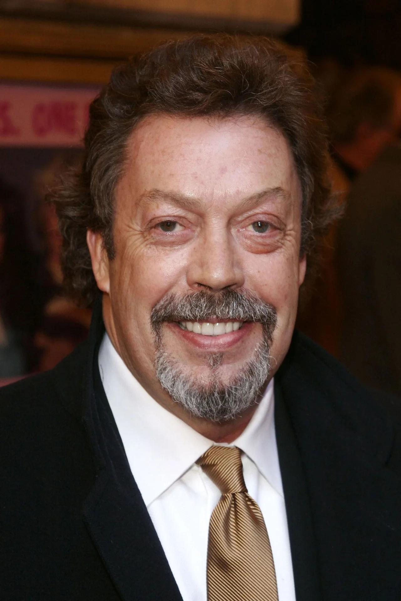 Homem em camiseta preta faz flexão, ao fundo pôster antigo de Tim Curry como Darkness em Legend