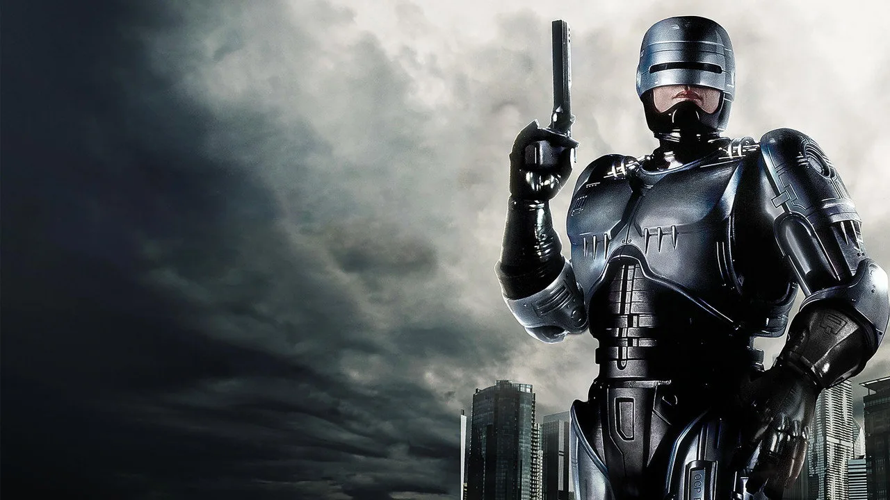 Homem musculoso segurando quadrinhos de RoboCop ao lado de um haltere, com pôsteres de filmes ao fundo