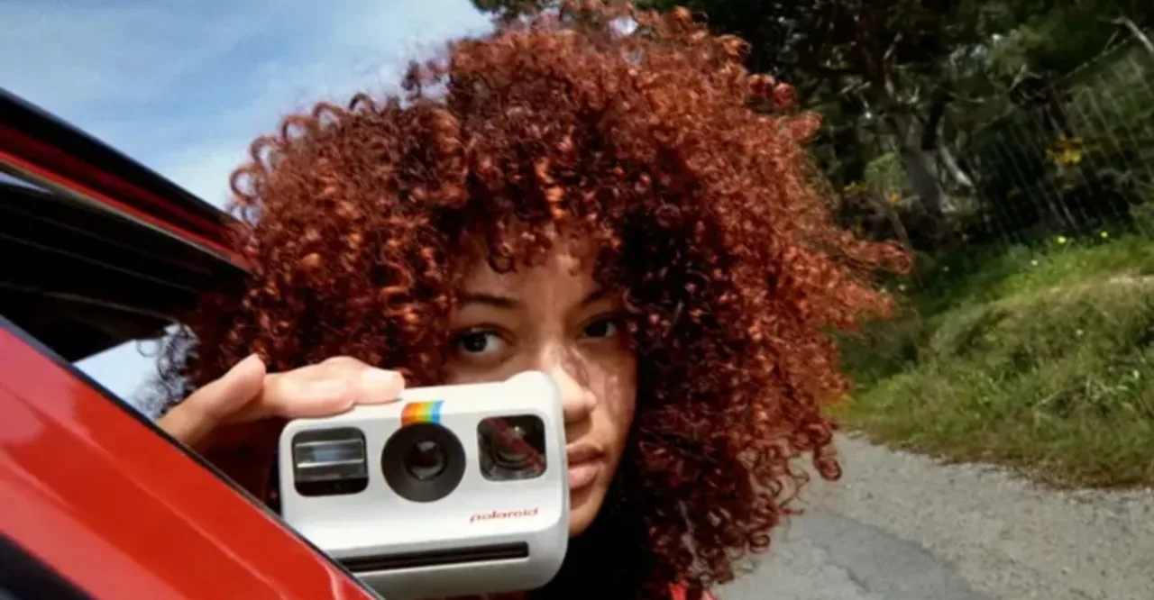 Jovem segurando a Polaroid Go ao lado de um smoothie verde e halteres coloridos