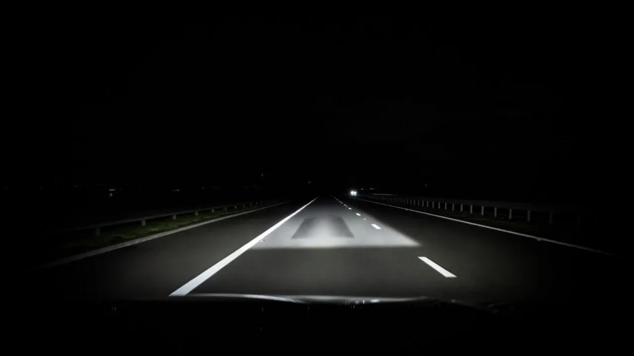 Close-up de faróis LED de um Audi Q9 iluminando uma estrada noturna com feixes de luz precisos e tecnologia ADB