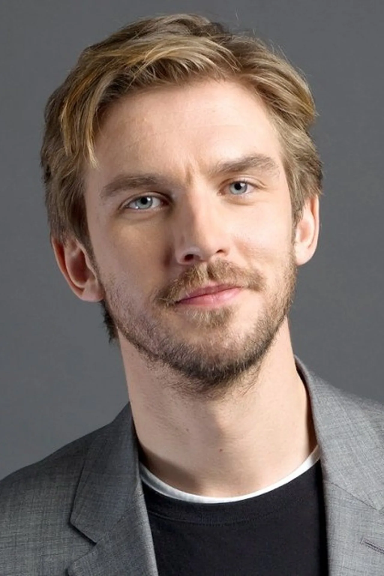 Ator Dan Stevens segurando um livro clássico ao lado de halteres e uma garrafa de água em um ambiente minimalista