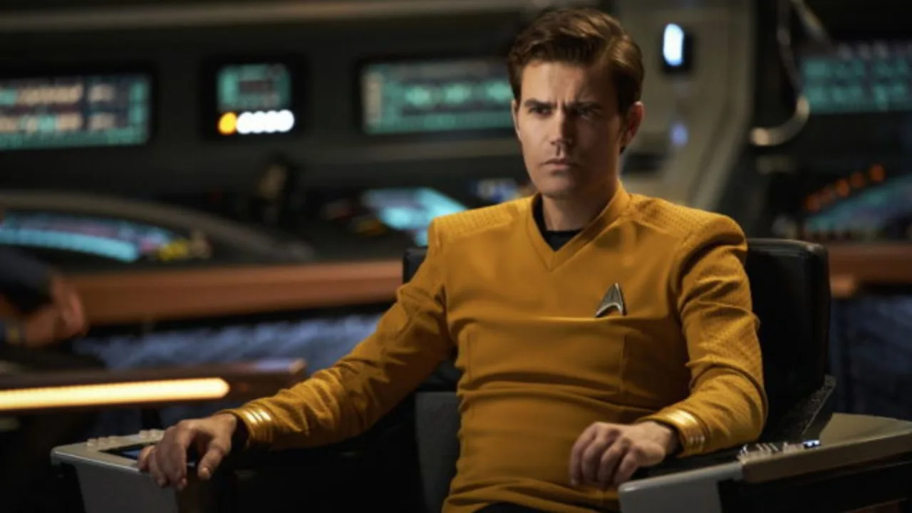 Pessoa em traje de astronauta da Star Trek fazendo flexão com halteres ao lado de um modelo de nave espacial