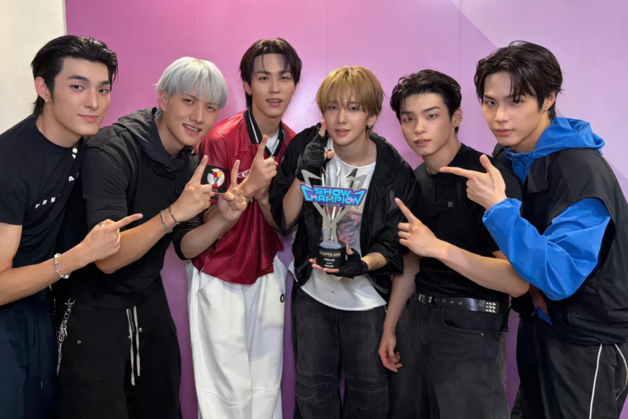 Membros de 82MAJOR erguendo o troféu do Show Champion no palco iluminado, com o logo do programa ao fundo