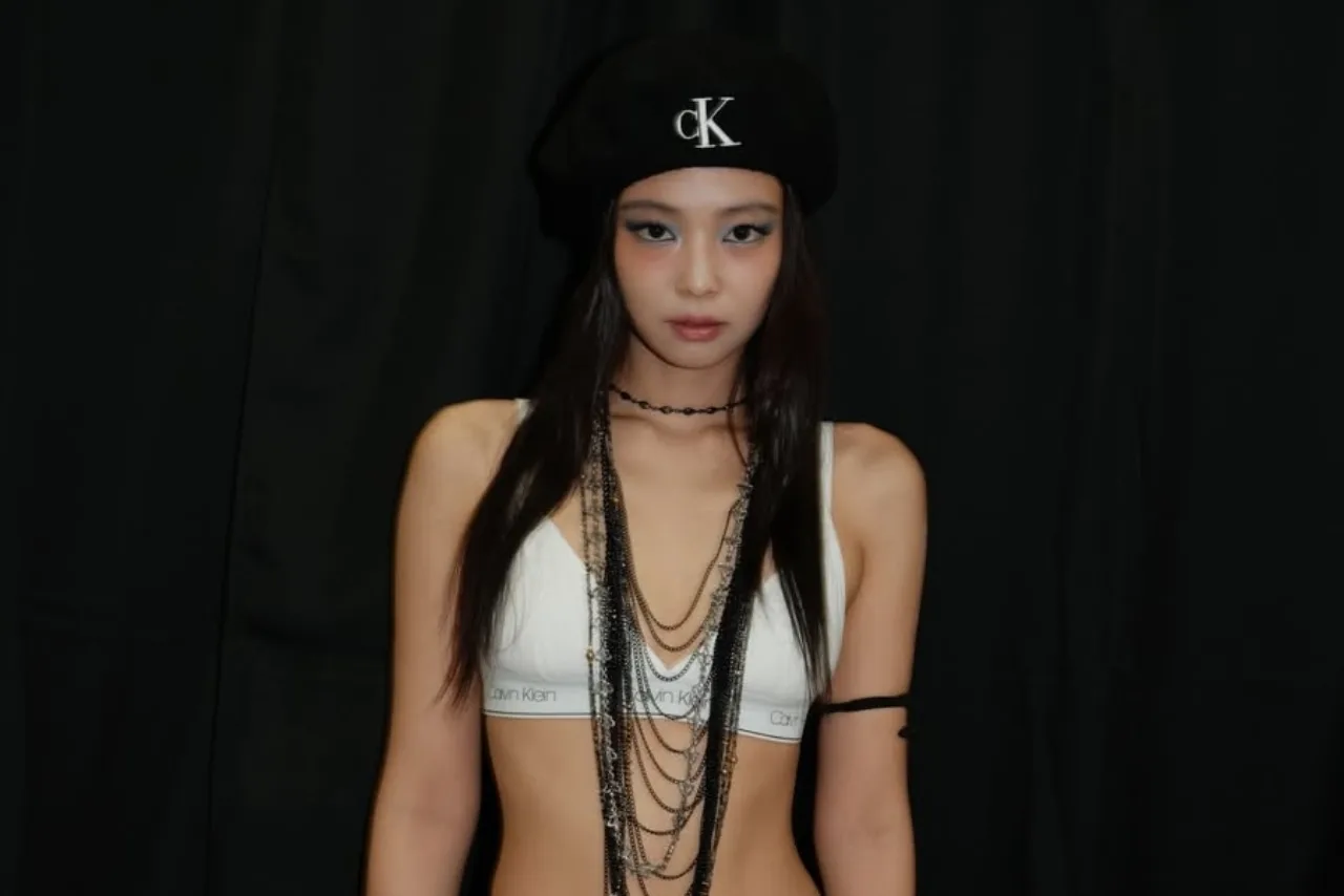 Jennie fazendo pilates no reformer, vestindo top e legging pretos, com garrafa d'água ao lado