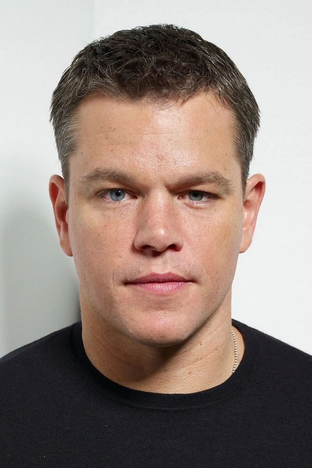Matt Damon levanta halteres de metal em banco de supino com toalha branca no pescoço e garrafa de água ao lado