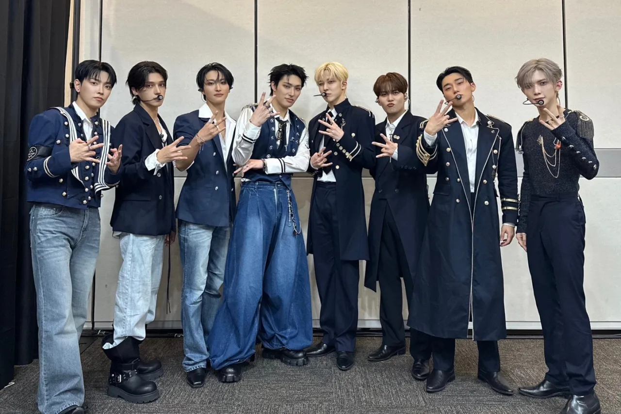 Jovens fazendo agachamento ao som de ATEEZ, usando fones, camiseta temática, garrafa de água e halteres