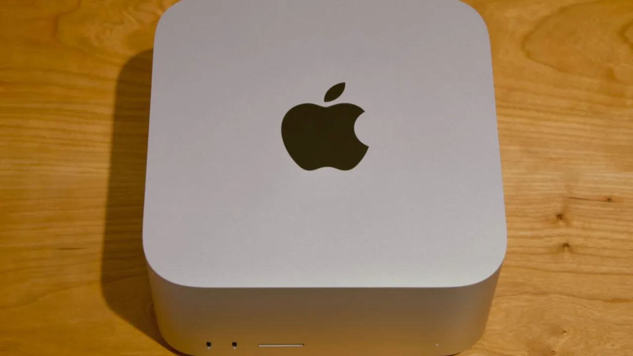 Mac Studio M5 Ultra e M1 Ultra lado a lado sobre mesa, com teclado, cabo de energia e logo da Apple ao fundo