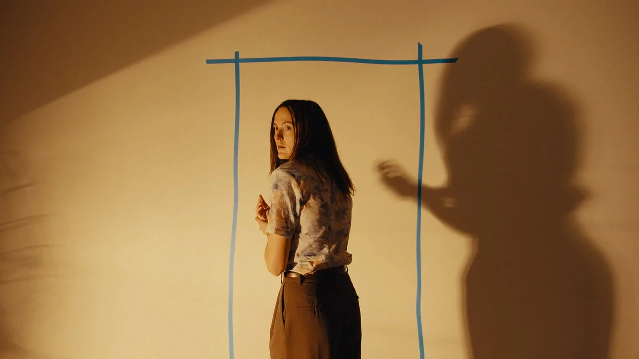 Jovem em leggings faz agachamento ao lado de pôsteres de Annihilation, Arrival e Duna, segurando garrafa d’água
