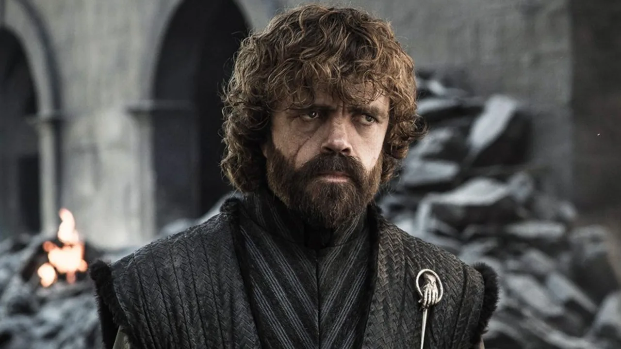 Homem musculoso segurando halteres ao lado de um dragão de brinquedo, vestindo camiseta com brasão dos Lannister