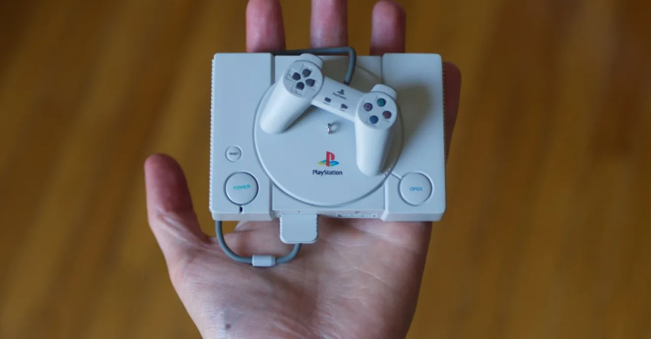 Um jovem em roupa de treino levanta halteres enquanto segura o console replica do PlayStation ao lado