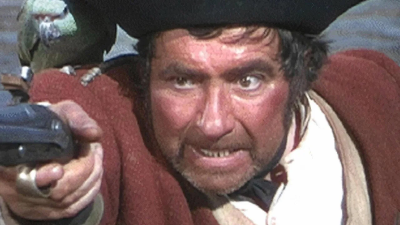 Homem em traje de ginástica levanta halteres ao lado de pôster de Treasure Island e logo de Alien
