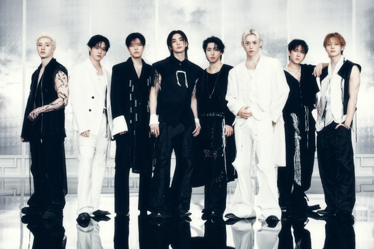 Membros do Stray Kids posam ao lado do troféu Grammy e do logotipo da JYP, com expressão de surpresa