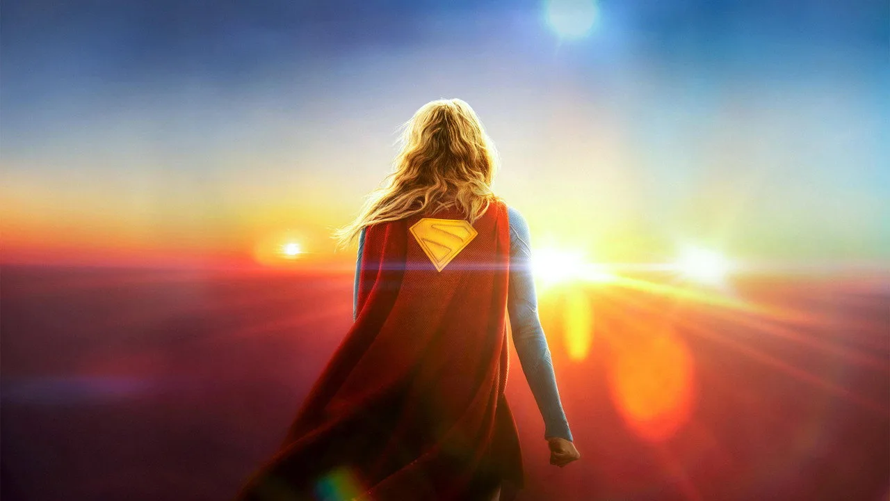 Jovem vestindo camiseta da Supergirl faz agachamento com halteres ao lado de TV exibindo o filme