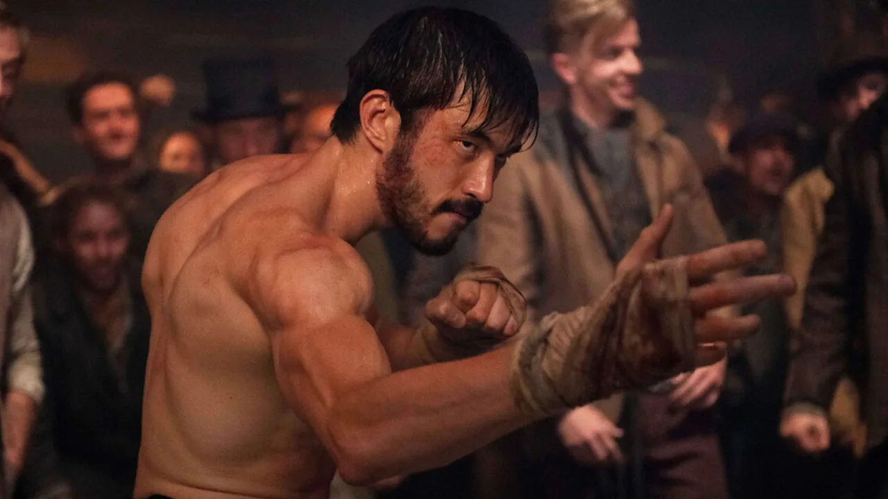 Praticante de artes marciais em uniforme preto, executando chute alto ao lado de saco de pancadas e kettlebell
