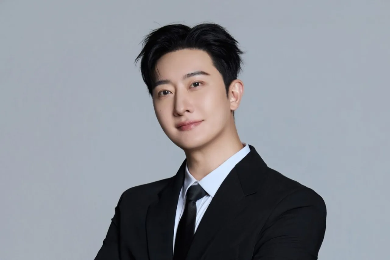 Zhoumi em roupa esportiva, fazendo agachamento ao lado de um notebook aberto com logotipos da SM e Tencent