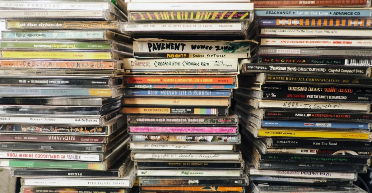 Jovem correndo na esteira, fones de ouvido e caixa de CD de banda indie ao lado da garrafa de água