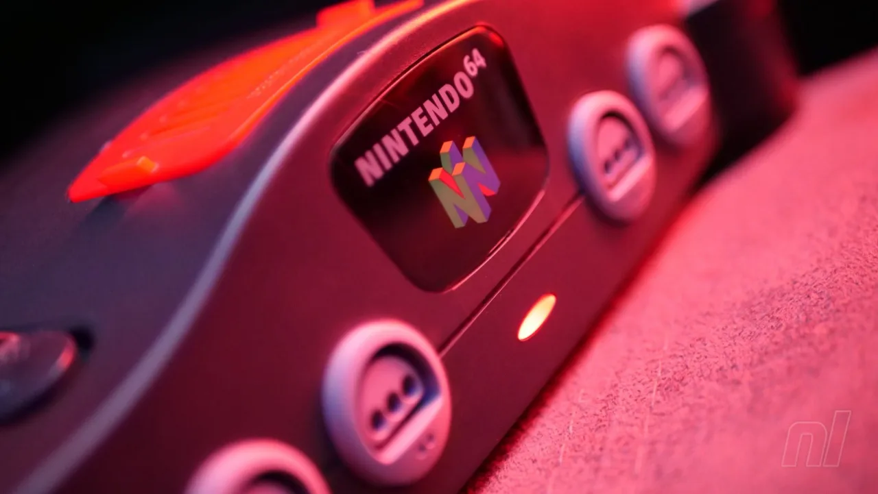 Jovem sentado no sofá, segurando controle N64, cercado de latas de refrigerante e pacote de batata chips