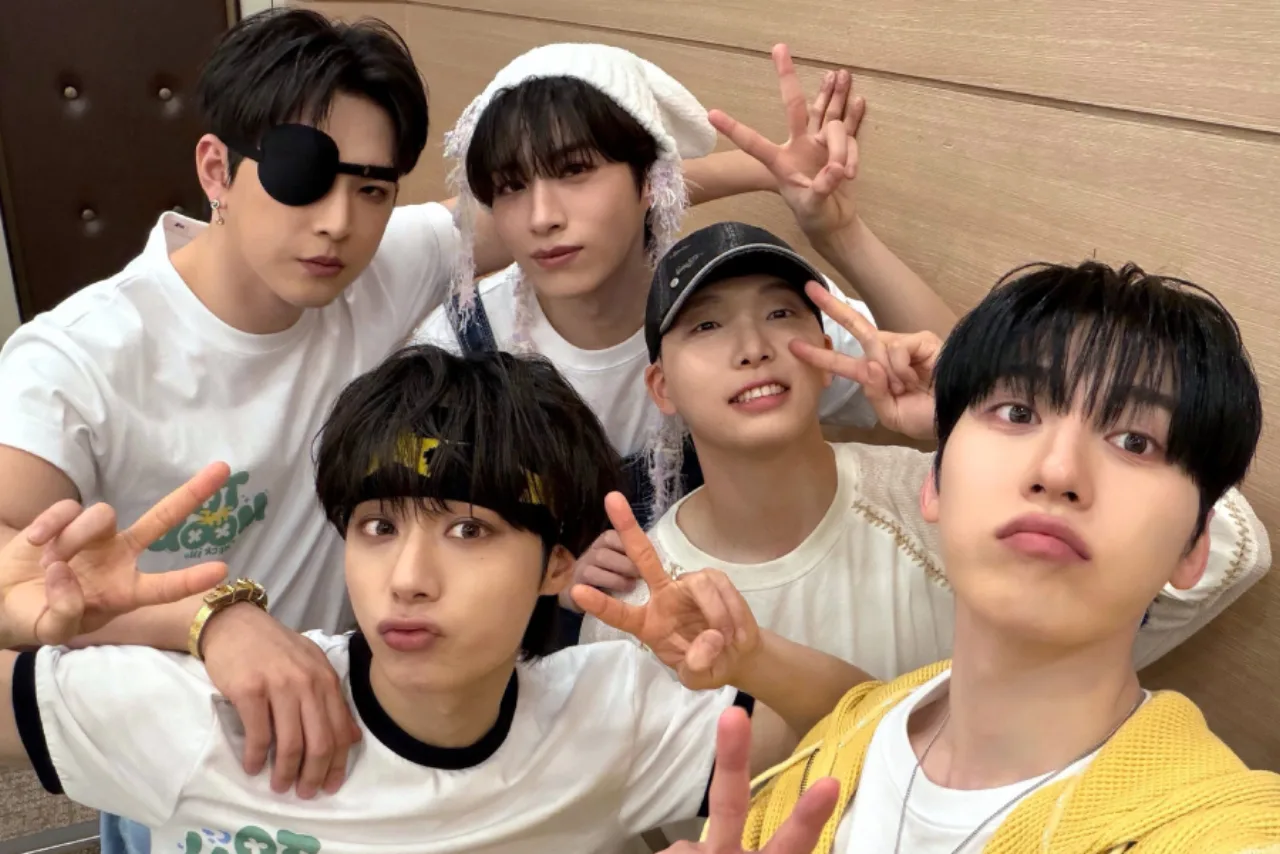 Jovem vestindo roupa de treino faz coreografia K‑pop com fones, ao lado de garrafa d'água e tapete de yoga
