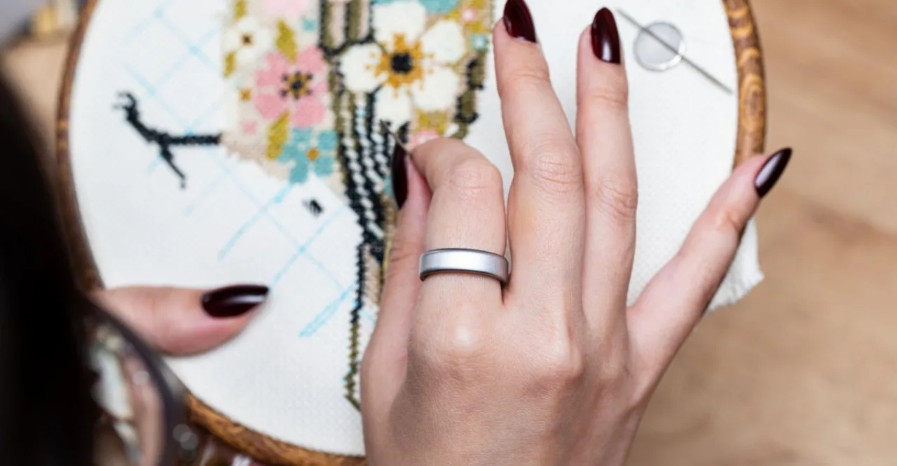 Pessoa em roupa de treino segurando o celular que exibe o app da Oura, com o Oura Ring 5 brilhando no dedo indicador
