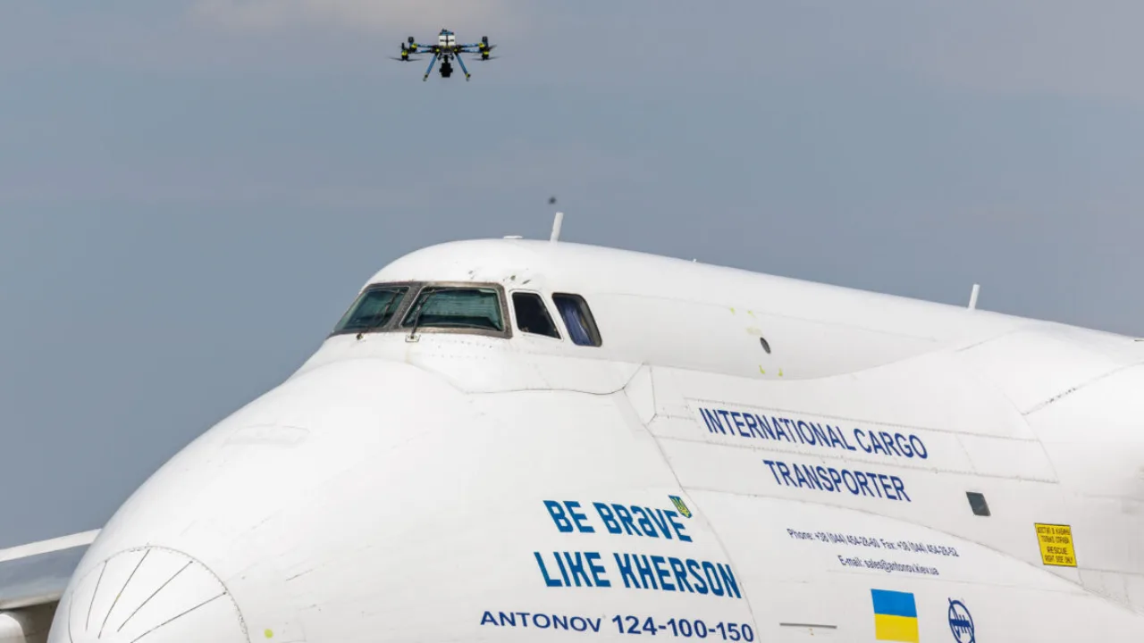 Atleta em uniforme de corrida, segurando garrafa de água, observa drones sobre pista de aeroporto