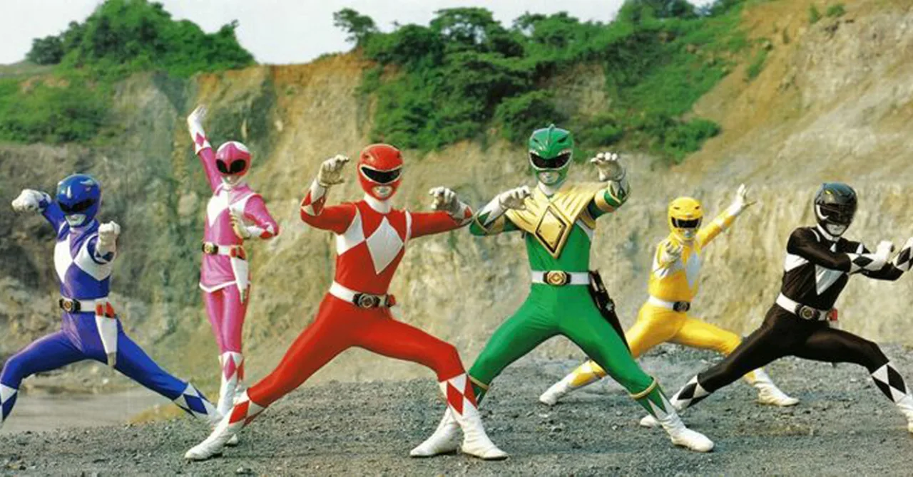 Jovem vestindo camiseta dos Power Rangers faz agachamento segurando halteres vermelhos ao lado de caixas de brinquedo
