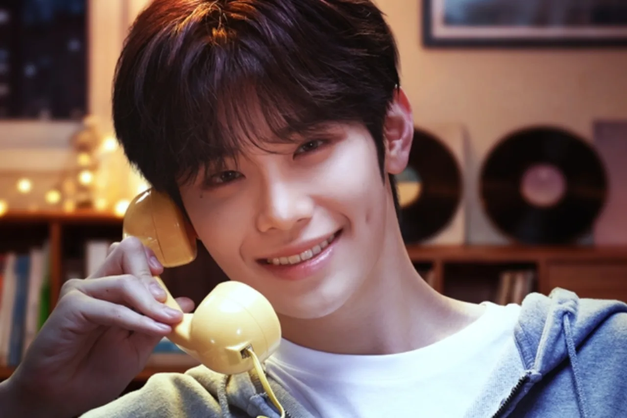Kim Tae Rae segurando fones, ao lado de halteres e garrafa de água, vestindo roupa esportiva em estúdio de rádio