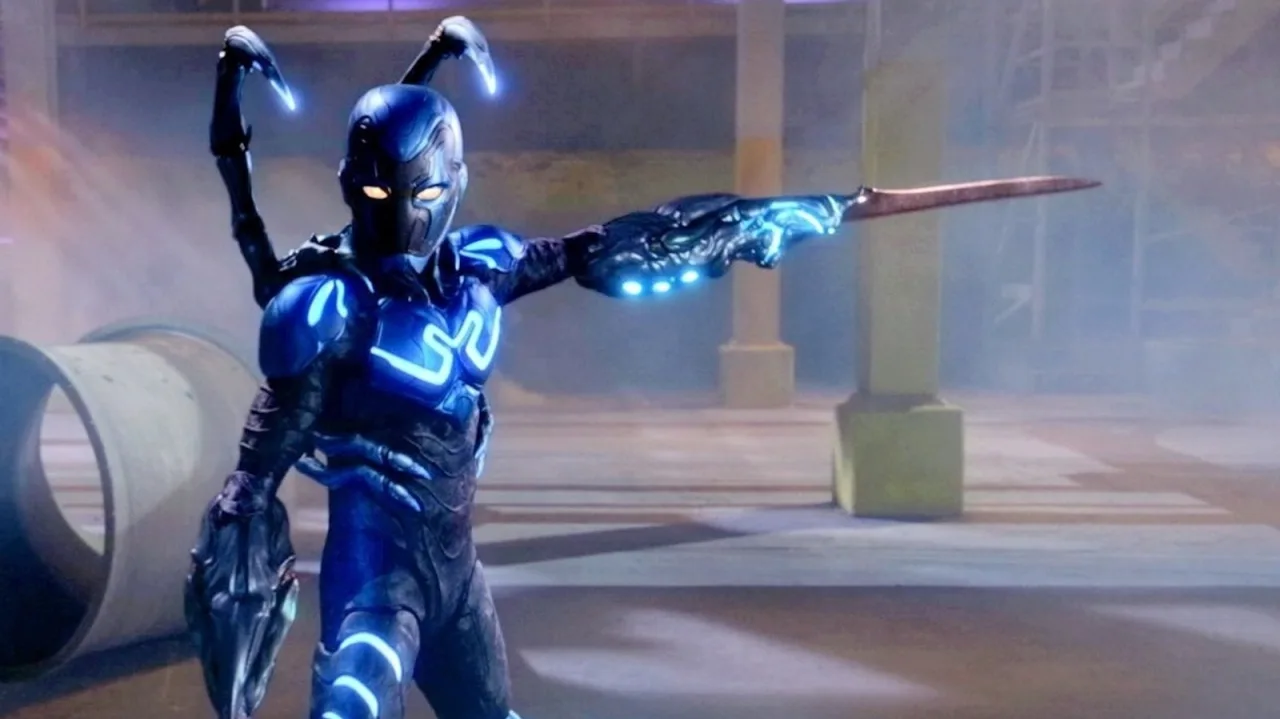 Xolo Maridueña vestindo roupa de treino, segurando halteres e usando o escaravelho azul iluminado