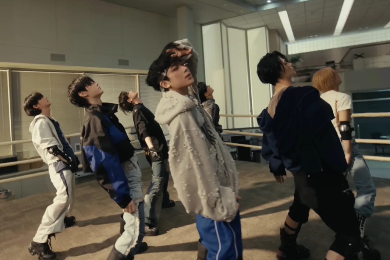 Jovens fazendo coreografia de K‑pop, suados, com garrafinhas d’água e laptop exibindo 100 mi de visualizações
