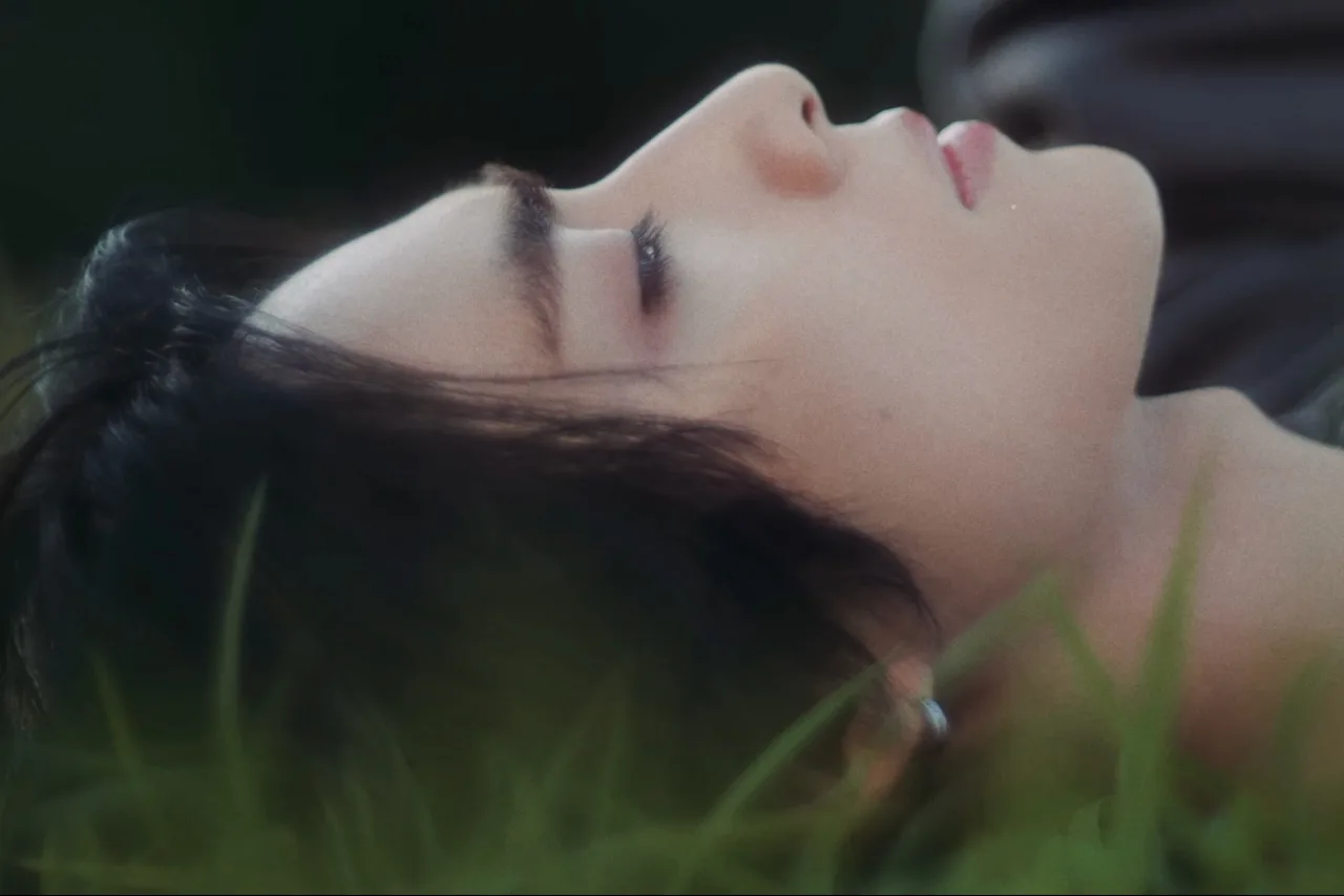Xiaojun aparece em close, vestindo roupa futurista, com luzes neon ao fundo e o título “Hey, Somebody” projetado