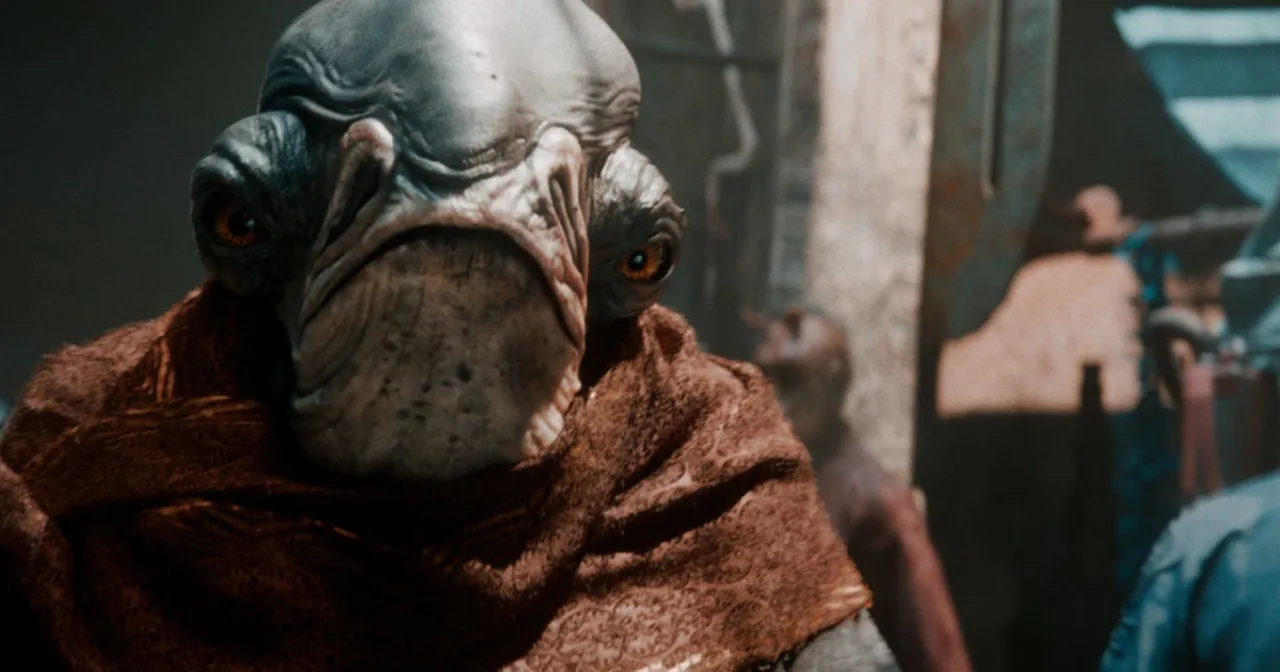 Um desenvolvedor de jogos suando, fazendo flexões ao lado de consoles, cabos e pôsteres de Star Wars