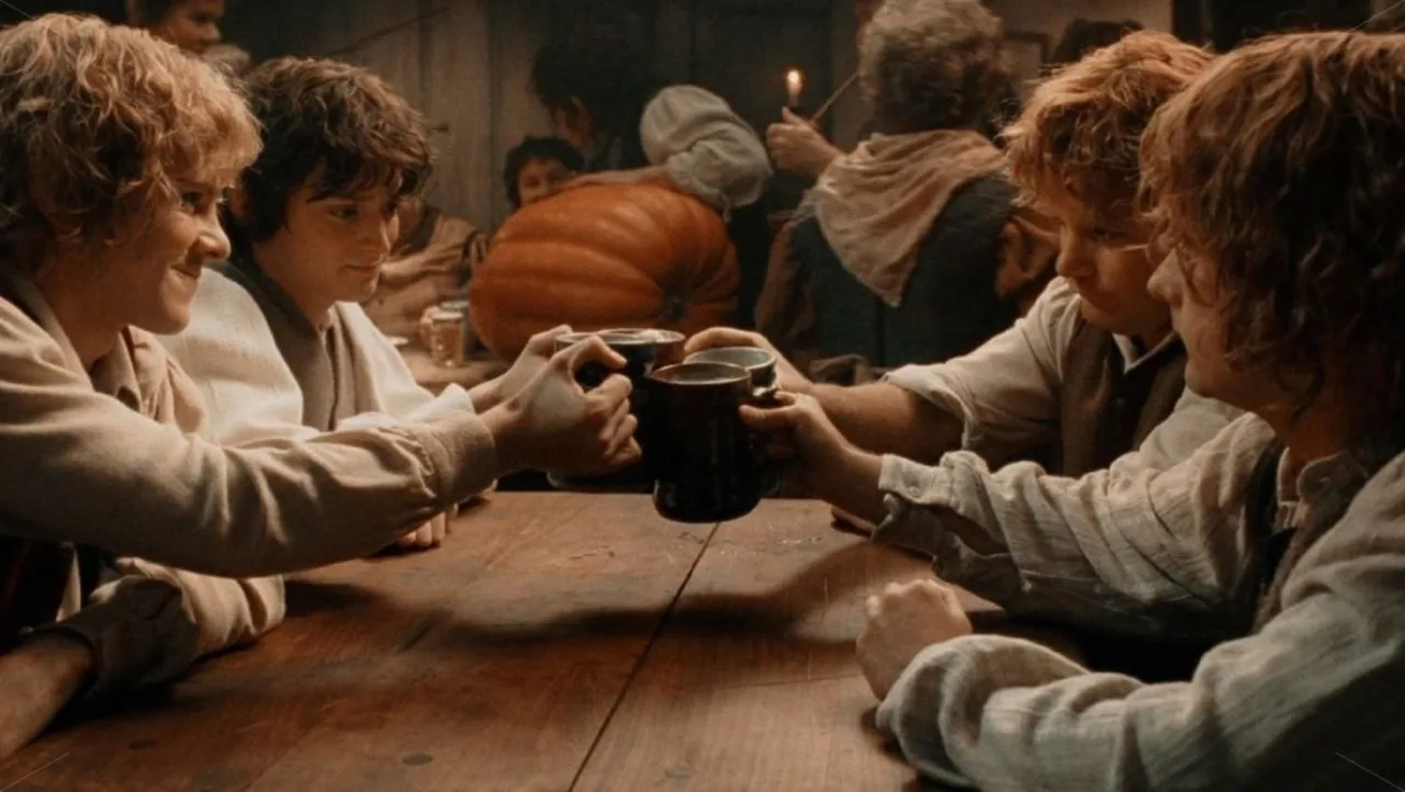 Bilbo e Frodo lado a lado, com um fundo de Hobbiton e o selo “Hobbit Day” sobre a paisagem da Terra‑média