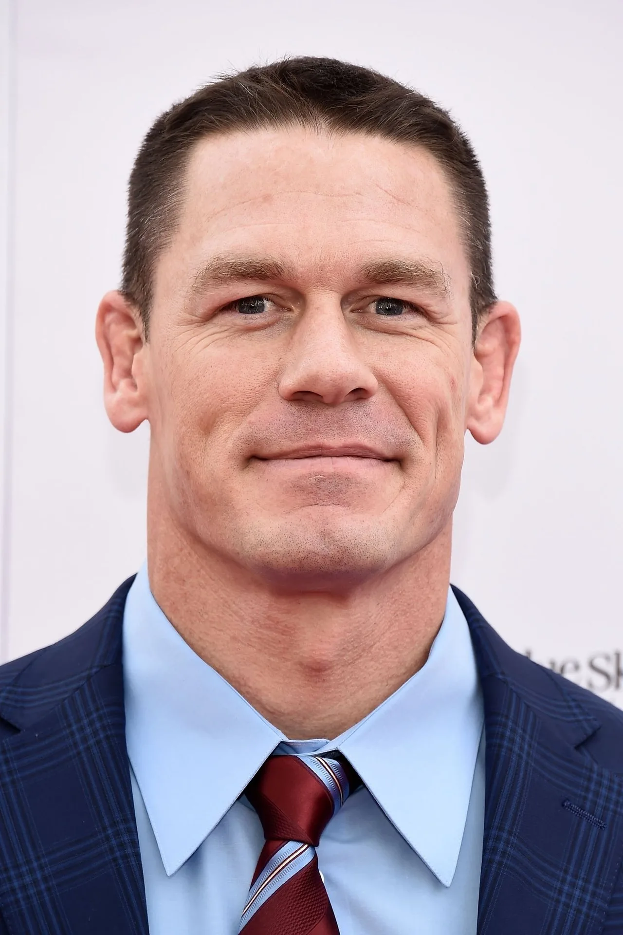 John Cena em roupa de treino, segurando halteres, ao lado de uma caixa de DVD de “Peacemaker”