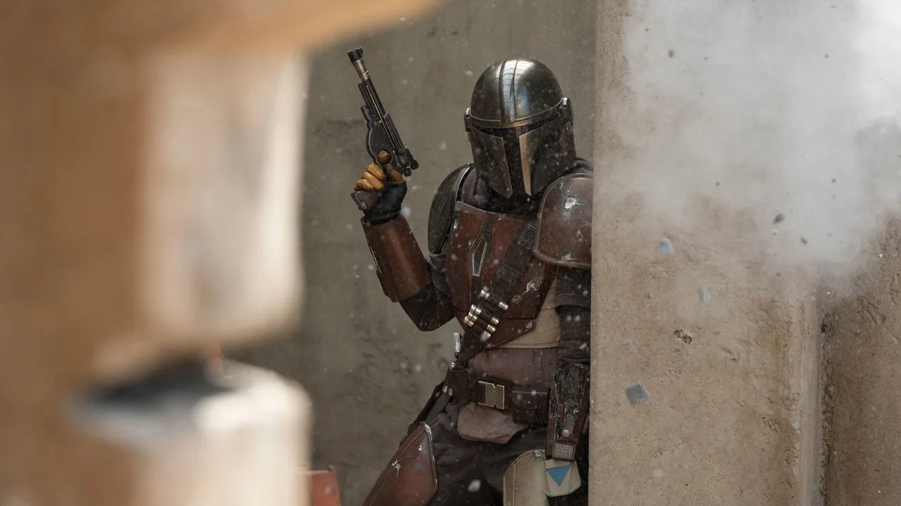 Jovem em roupa de treino faz agachamento segurando um sabre de luz azul ao fundo de pôster de The Mandalorian