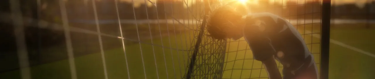 Jovem atleta em campo verde, vestindo chuteiras, driblando bola enquanto faz alongamento