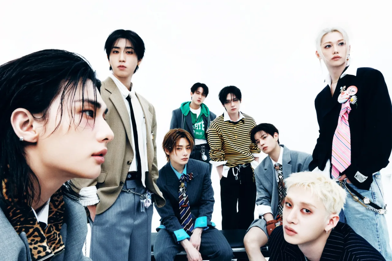 Membros do Stray Kids em pose triunfante, segurando discos dourados ao lado de um gráfico Billboard 200