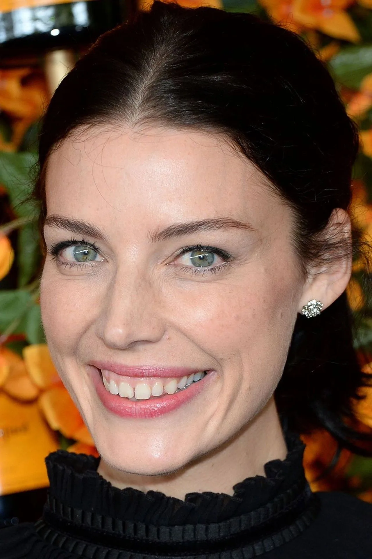 Jessica Paré vestindo roupa de treino, fazendo agachamento com halteres, ao lado de um tapete de yoga e garrafa d'água