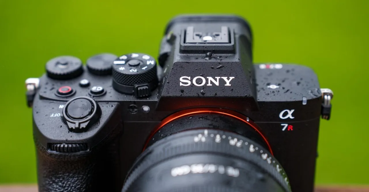 Corredor usando smartwatch, segurando a Sony A7R VI enquanto passa por trilha arborizada com garrafa de água