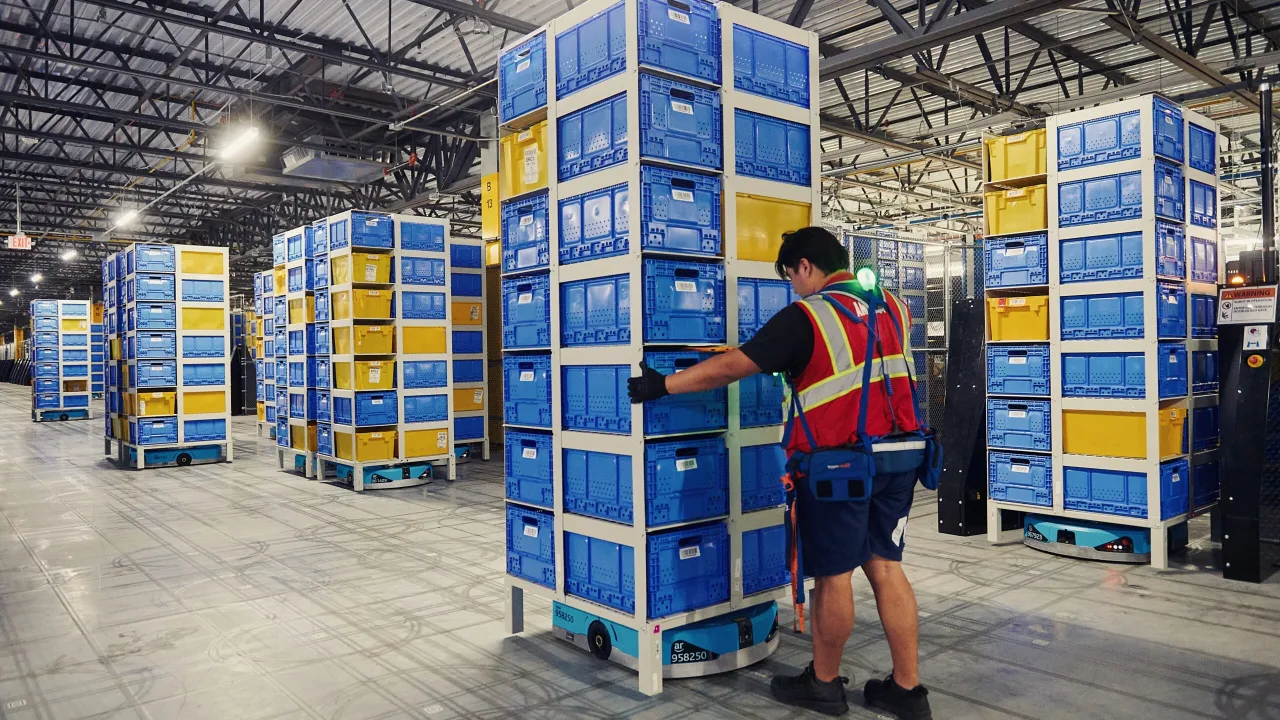 Robôs de estocagem da Amazon deslizam entre prateleiras enquanto funcionários observam o processo automatizado