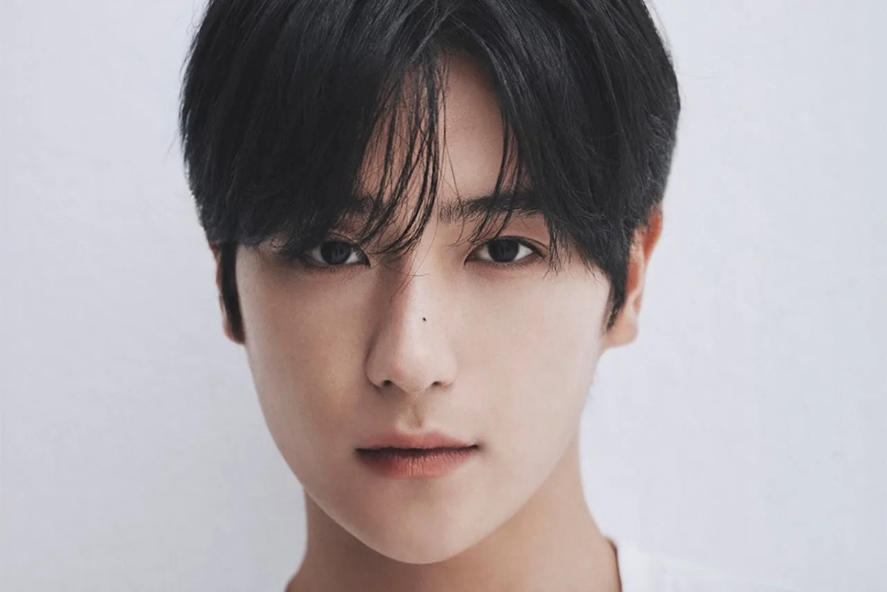 Hyunjae vestindo roupa de treino, segurando halteres, ao lado de uma garrafa d'água e um tapete de yoga