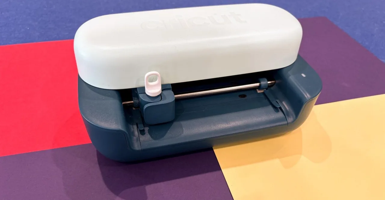 Halteres, garrafa de água com adesivo personalizado e a compacta Cricut Joy 2 sobre um tapete de ioga azul
