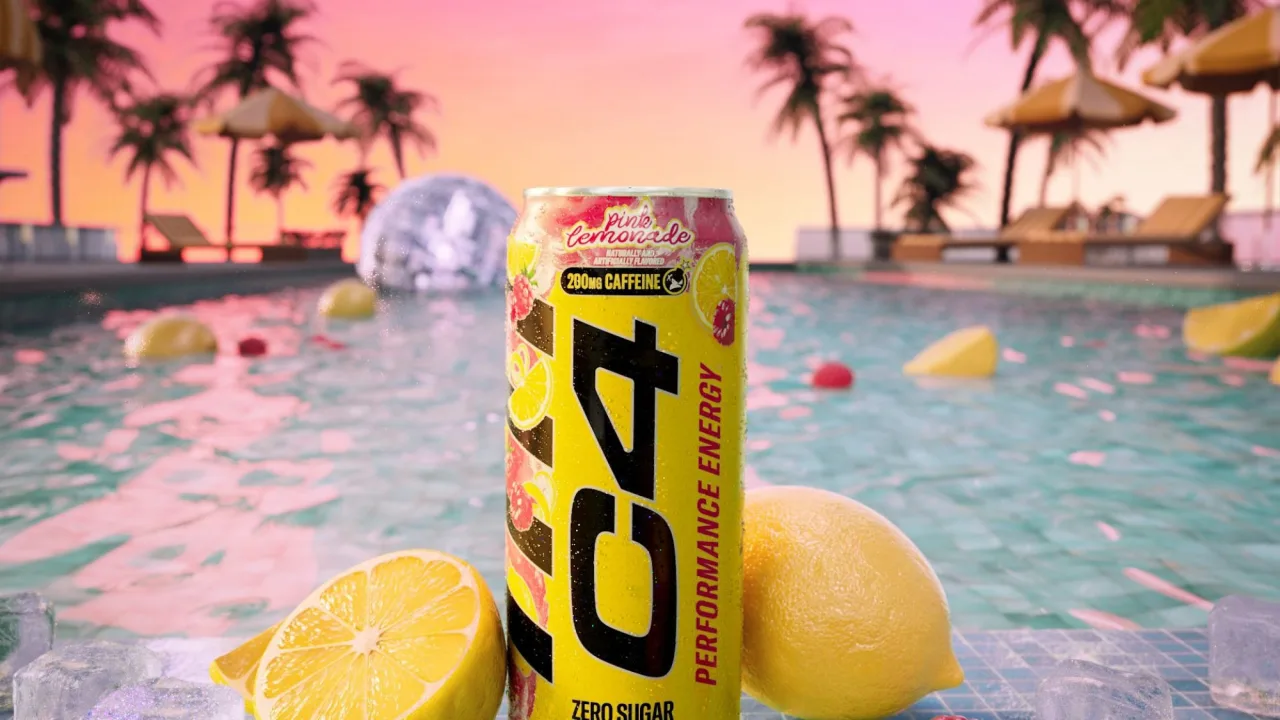 Lata de C4 Energy sabor Pink Lemonade sobre uma toalha de praia ao lado de halteres e óculos de sol sob o sol