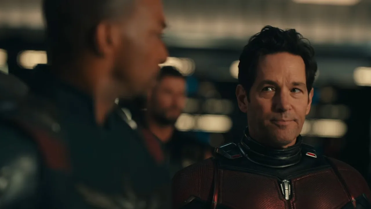 Ant‑Man ao lado do Capitão América, ambos em traje, com a logo de Avengers ao fundo, enquanto falam
