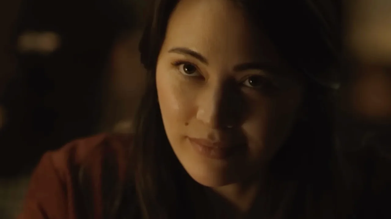 Jessica Henwick vestindo roupa esportiva, fazendo agachamento com halteres ao ar livre, ao pôr‑do‑sol